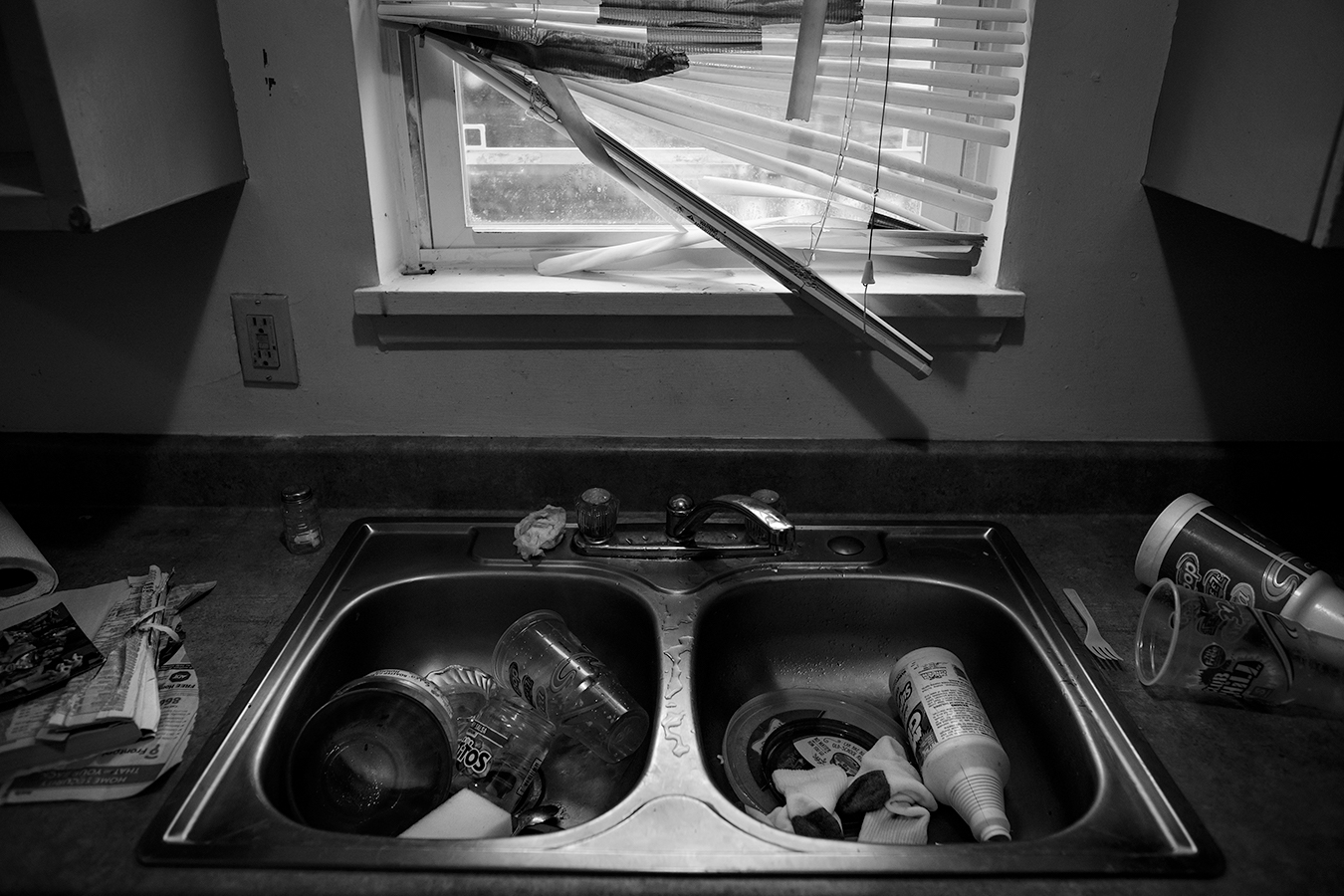 Broken blinds above a garbage-filled sink.