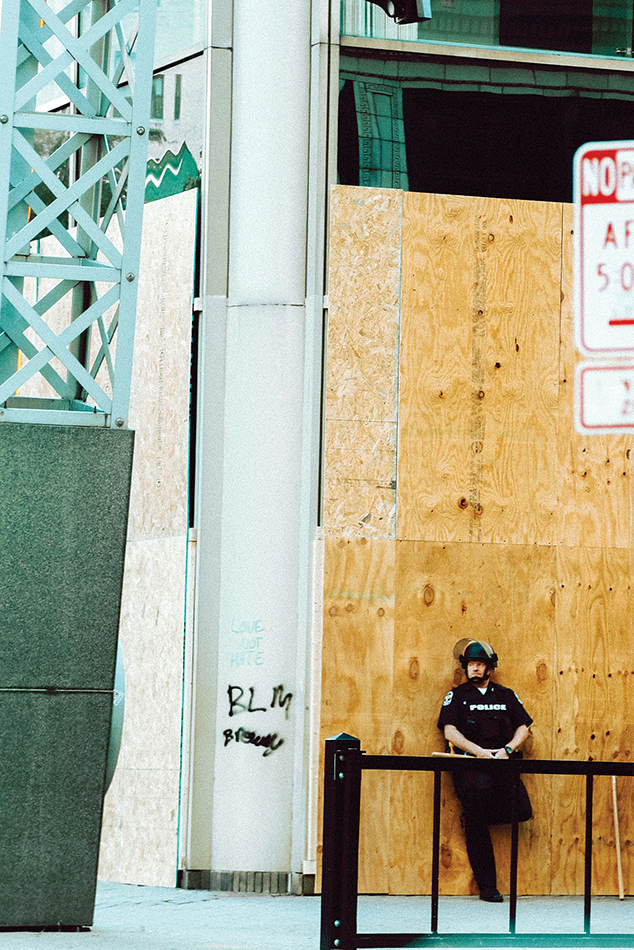 A police officer stands in front of plywood, near graffiti reading "BLM."